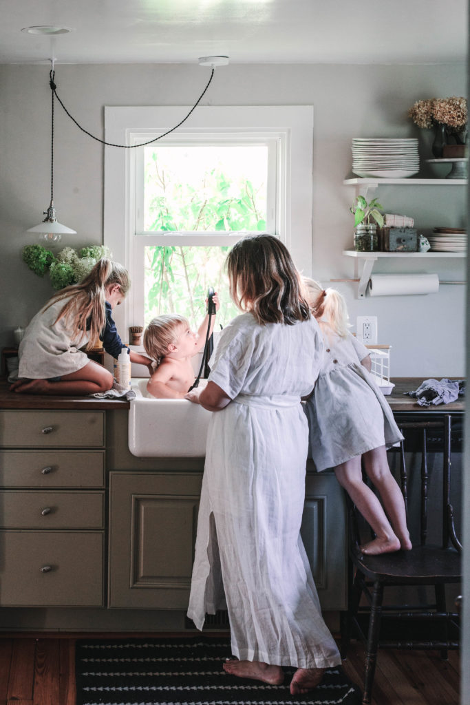 Mom and sisters giving baby brother a bath in the farmhouse kitchen sink