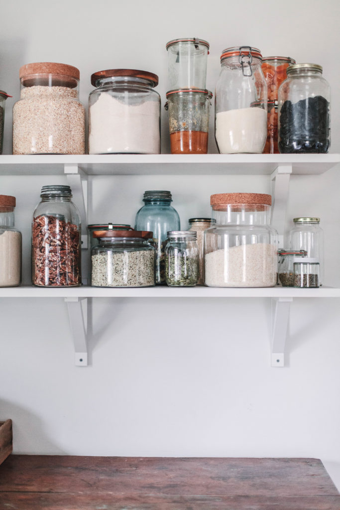 An open pantry shelf with jars of dry goods.