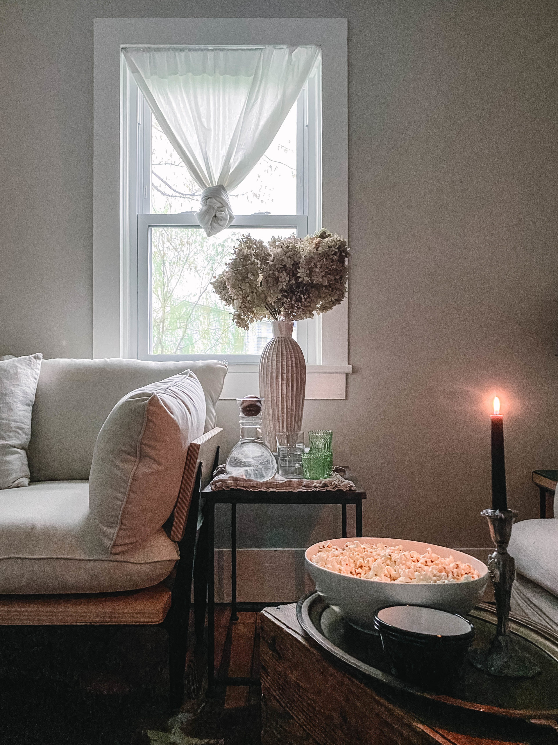 Cozy living room image with a candle lit, bowl of popcorn, drinks on side table.