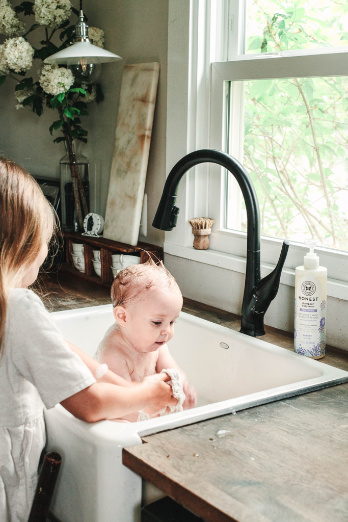 Girl giving her baby sister a bath in a sink