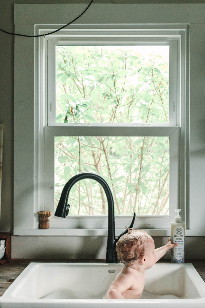 Baby having a bath in a farmhouse sink reaching for body wash